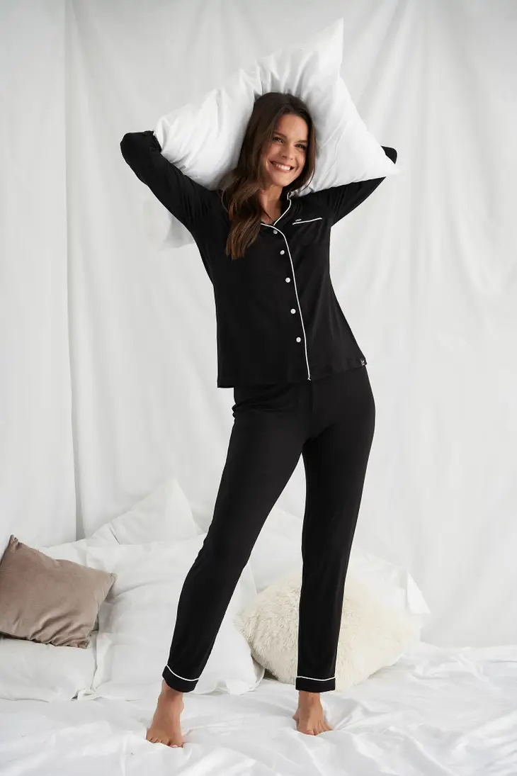 Model wearing black bamboo pajama pant set. White piping details with buttons and front pocket