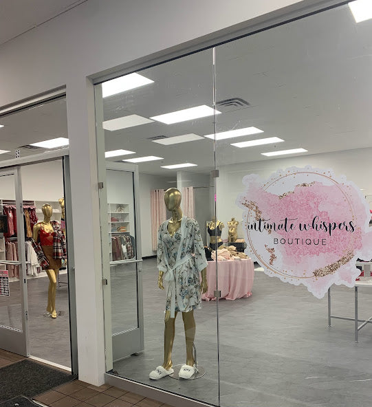 Boutique interior with mannequins and 'Intimate Whispers Boutique' sign.