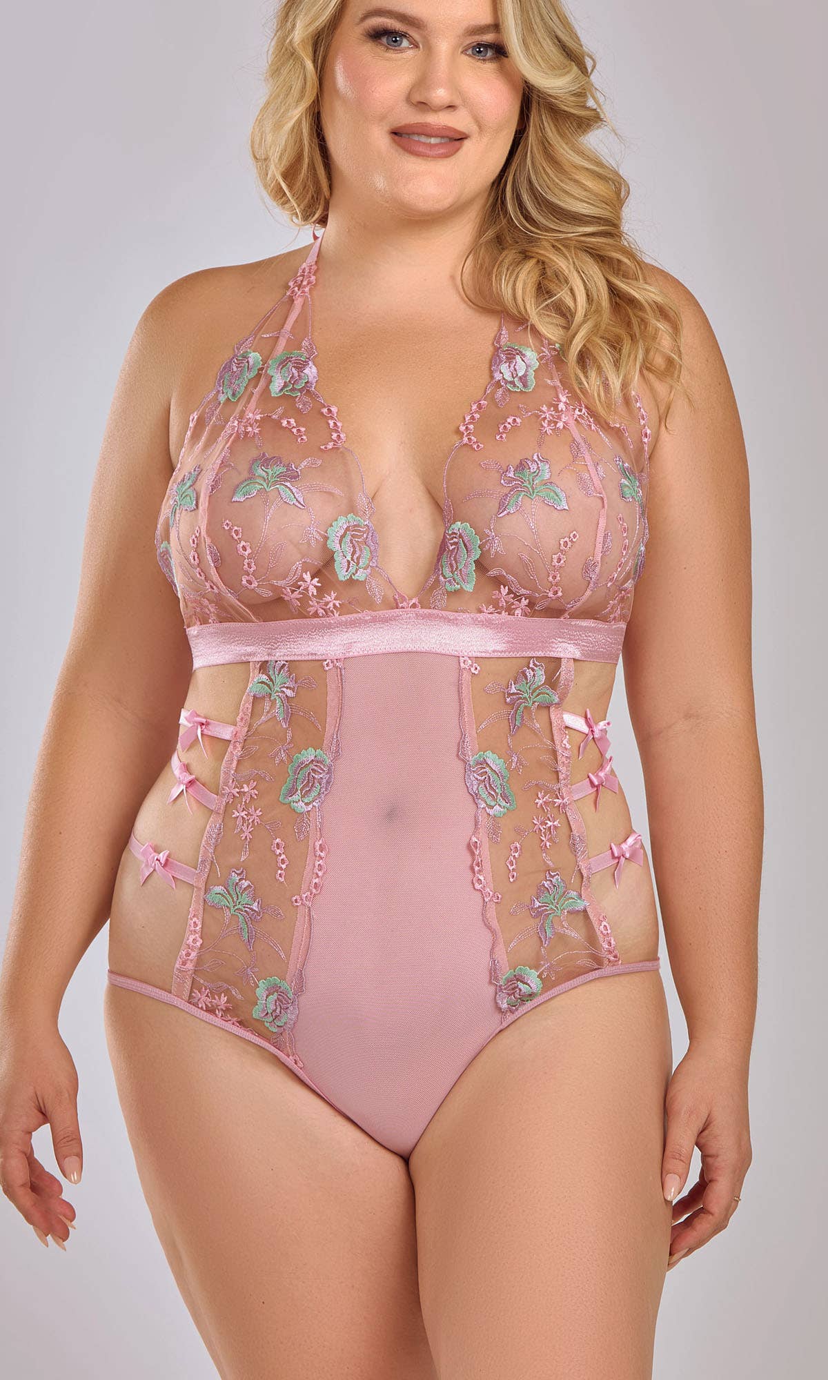 Women's pink floral embroidered lingerie bodysuit with side bows on plus size model
