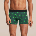 Men's boxer briefs, designed with both style and comfort in mind. The briefs are green, adorned with a pattern of white cannabis leaves, and include a black elastic waistband.